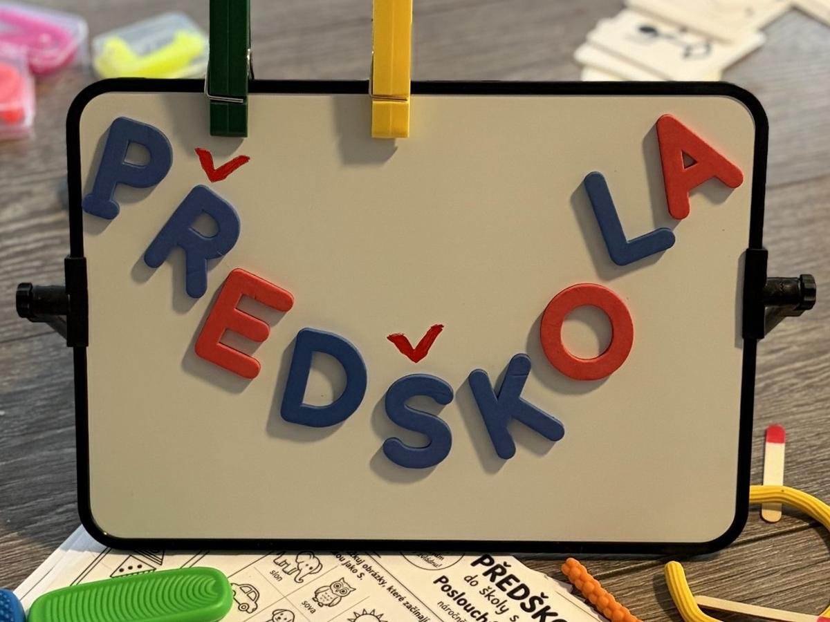 Magnetická tabule s nápisem PŘEDŠKOLA a pomůcky kolem ní